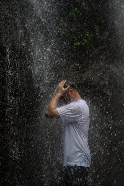 A man enjoying the refreshing splash of a waterfall, captured in a serene outdoor setting in Indonesia.